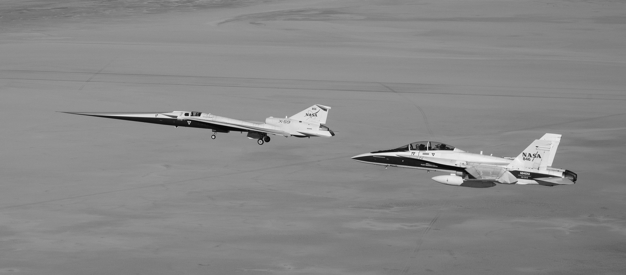 An experimental research aircraft in flight alongside a chase jet over open desert