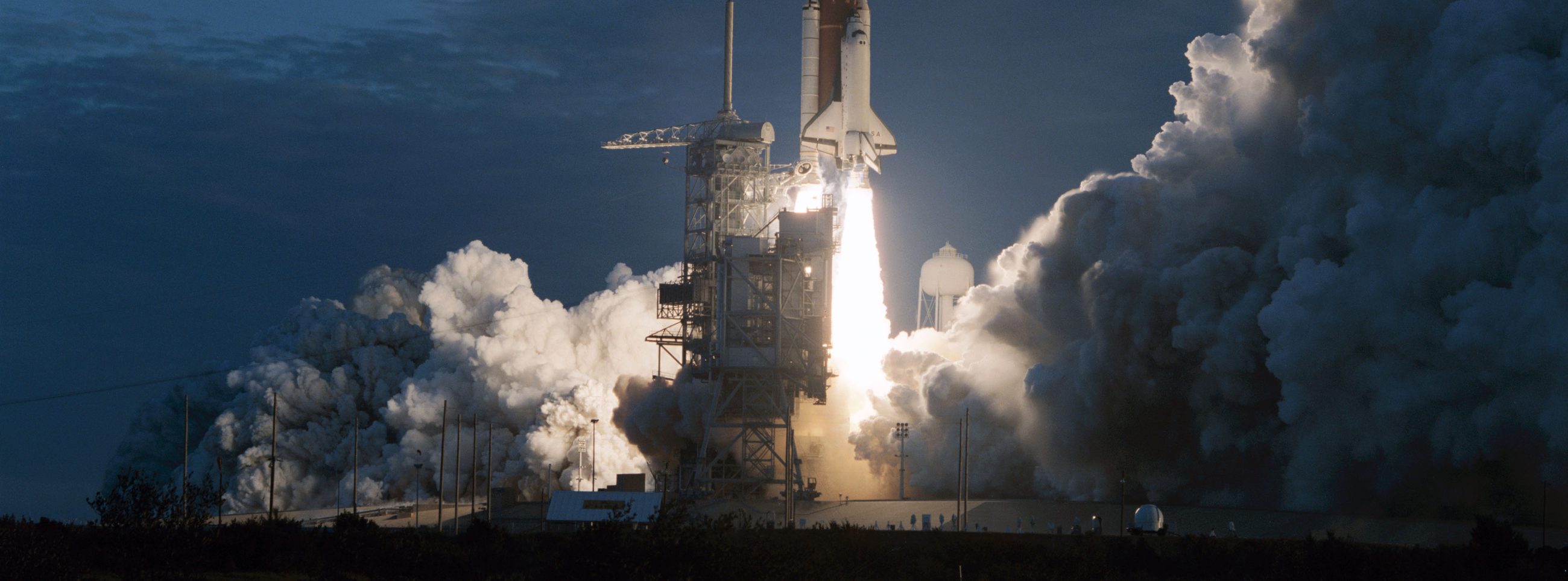 A launch vehicle lifting off at dusk, its exhaust lit against a deep blue sky