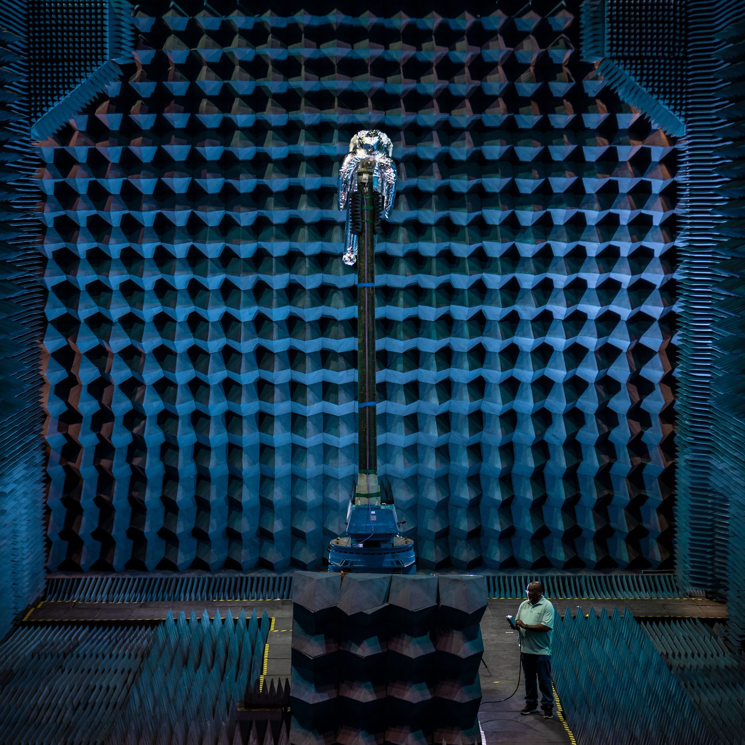 A figure standing inside a large anechoic chamber, dwarfed by walls of absorber cones